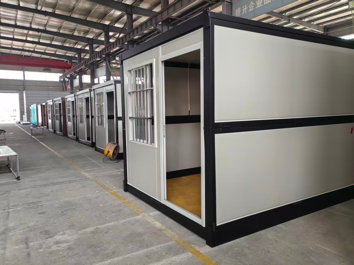 A modular two-story container office or restroom unit with white panels and black trim, shown in a warehouse with other similar units lined up in the background.