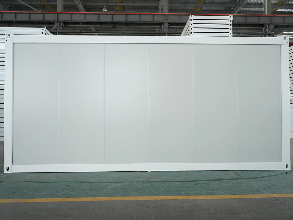 A large white modular partition wall panel with a white frame, standing upright in a warehouse or factory setting with industrial ceiling structures and a concrete floor visible.
