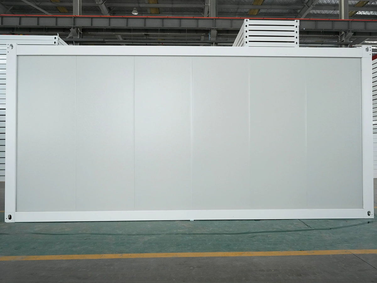 A large white modular partition wall panel with a white frame, standing upright in a warehouse or factory setting with industrial ceiling structures and a concrete floor visible.
