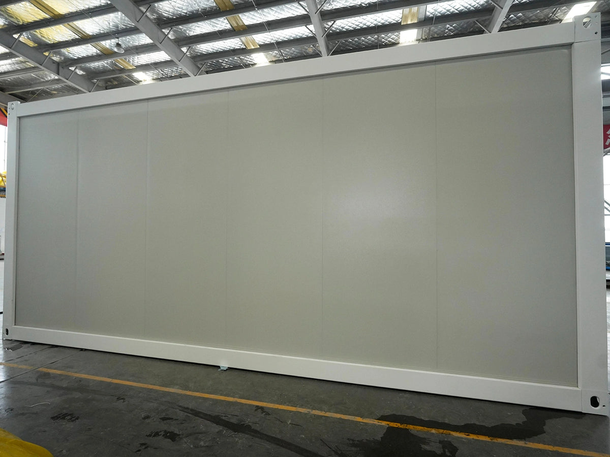A large white modular partition wall or storage cabinet panel system photographed in an industrial warehouse setting with metal roof beams and concrete floor visible.