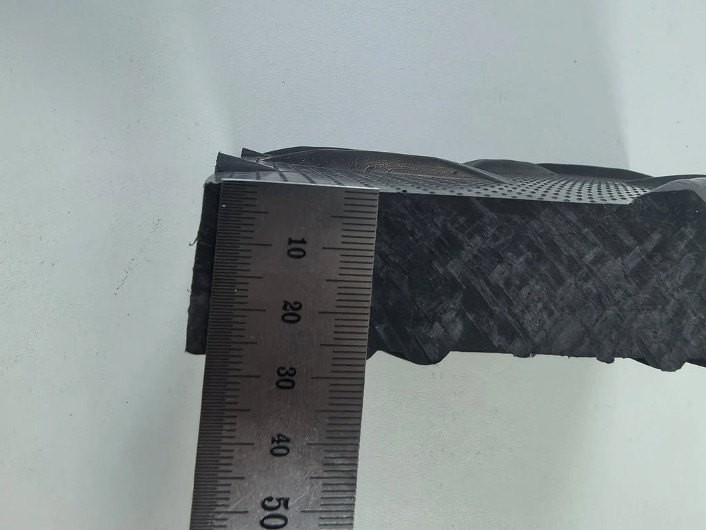 Close-up of a black textured object with a ruler for scale on a white background HDPE ROAD MATS 7