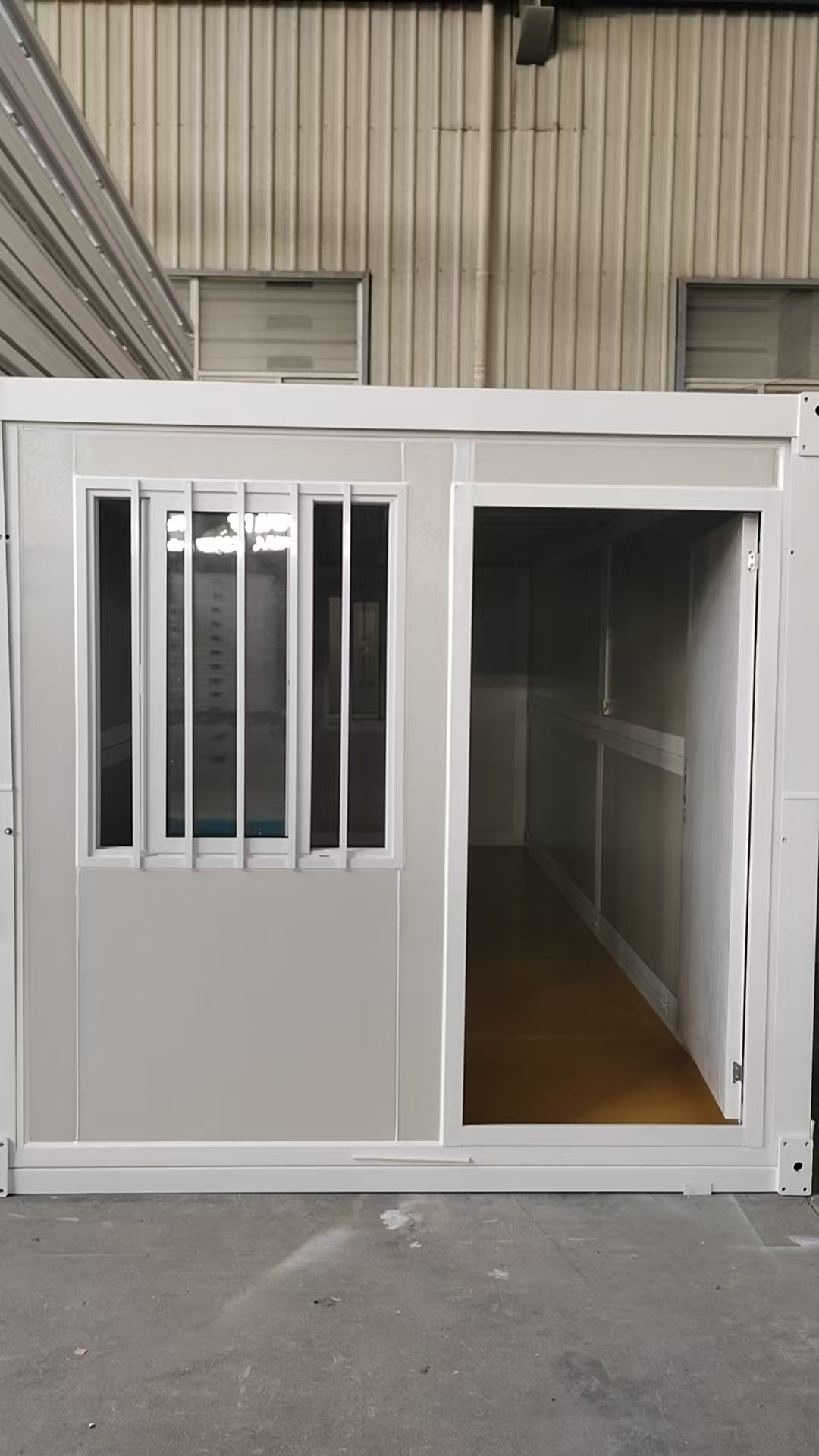 Small modular building with a door and window, attached to a larger structure.