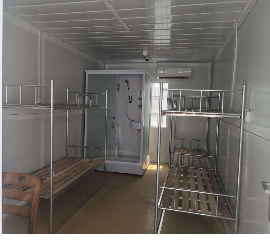Small room with metal bunk beds, a shower stall, and a bench.
